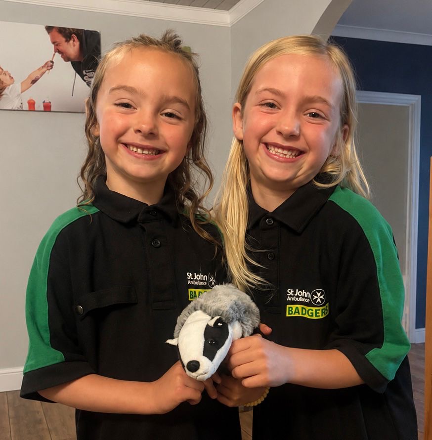 Two young St John Ambulance volunteers in branded polo shirts holding a toy badger